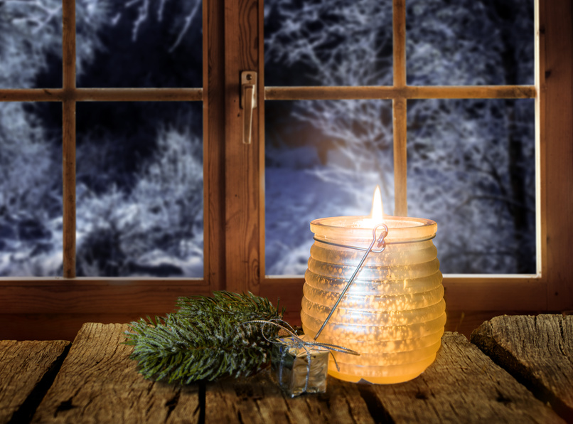 Kerzenlicht an einem Fenster vor verschneitem Winterwald im Advent